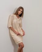 Woman facing the camera wearing crochet tan beige colored collared button up shirt with matching skirt 