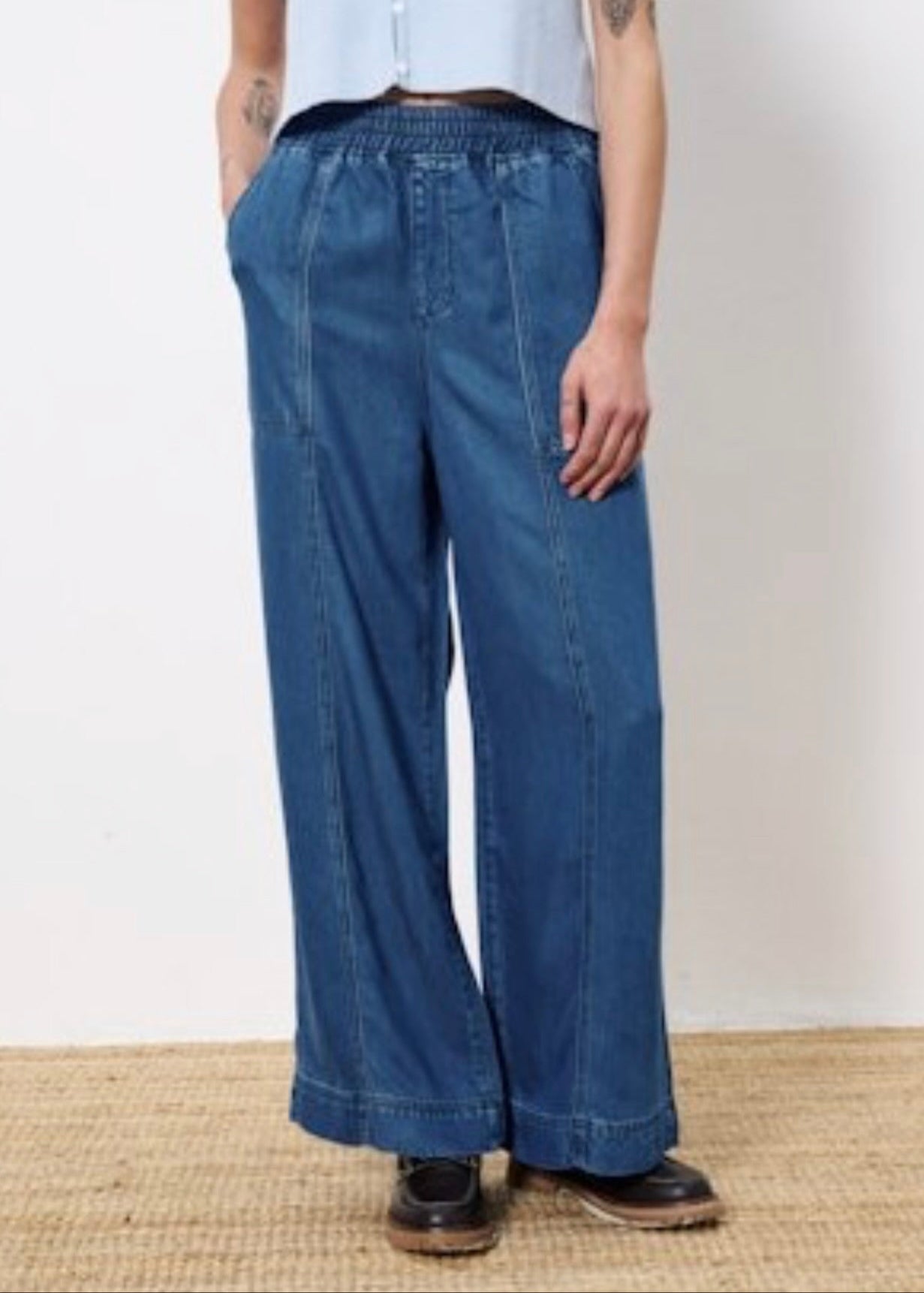 Woman wearing wide leg denim with elastic waistband, two front pockets, and two back patch pockets paired with light blue top and black shoes 