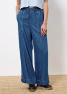 Woman wearing wide leg denim with elastic waistband, two front pockets, and two back patch pockets paired with light blue top and black shoes 