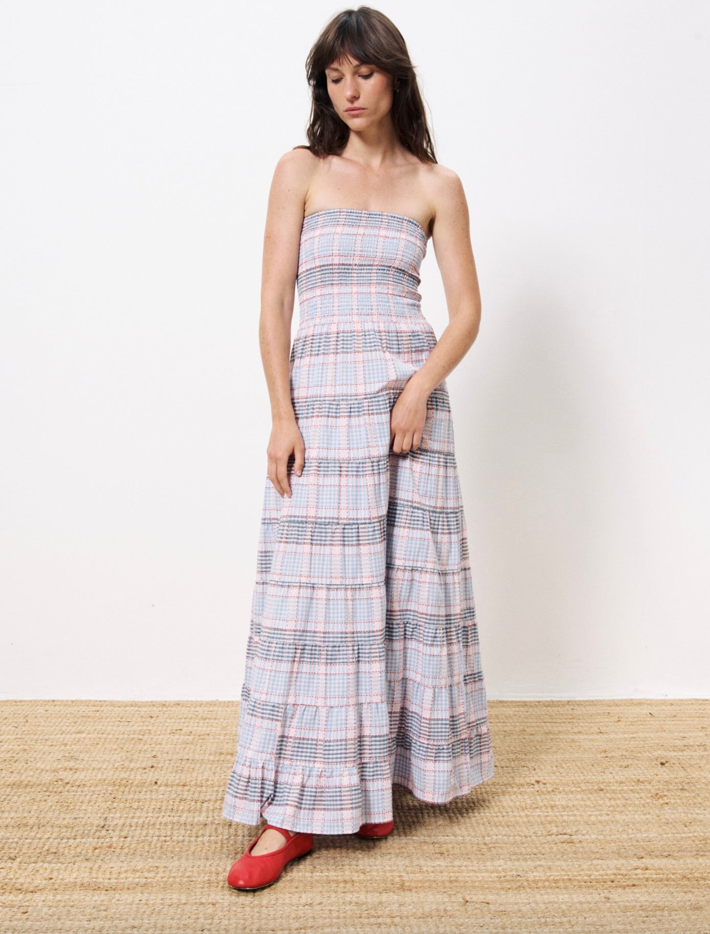 Woman wearing long red white and blue striped strapless dress, smocked on the chest paired with red ballet flats 