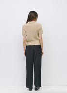 Woman facing backward wearing beige short-sleeve open knit top, collared neckline paired with black dress pants 