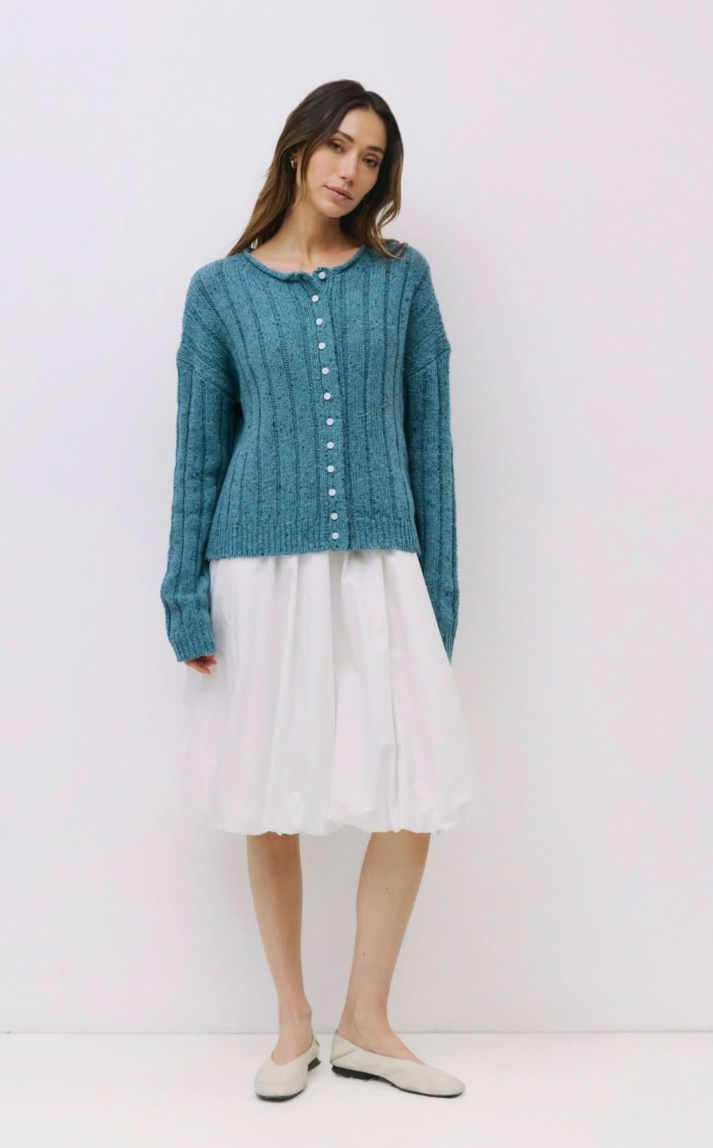 Woman wearing Blue specked chunky ribbed knit cardigan with rolled crewneck, dropped shoulders, relaxed fit paired with white skirt 