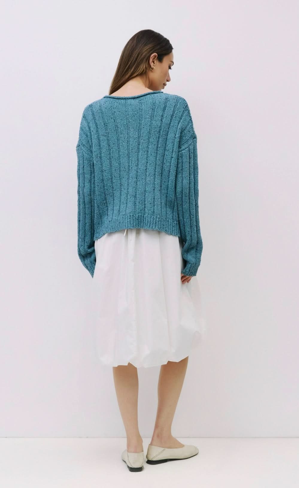Woman wearing Blue specked chunky ribbed knit cardigan with rolled crewneck, dropped shoulders, relaxed fit paired with white skirt 