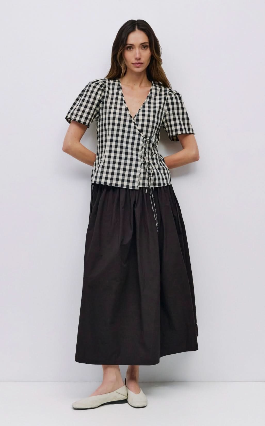 Woman wearing checkered puff sleeve blouse with 2 wrap ties in the front with black long skirt  