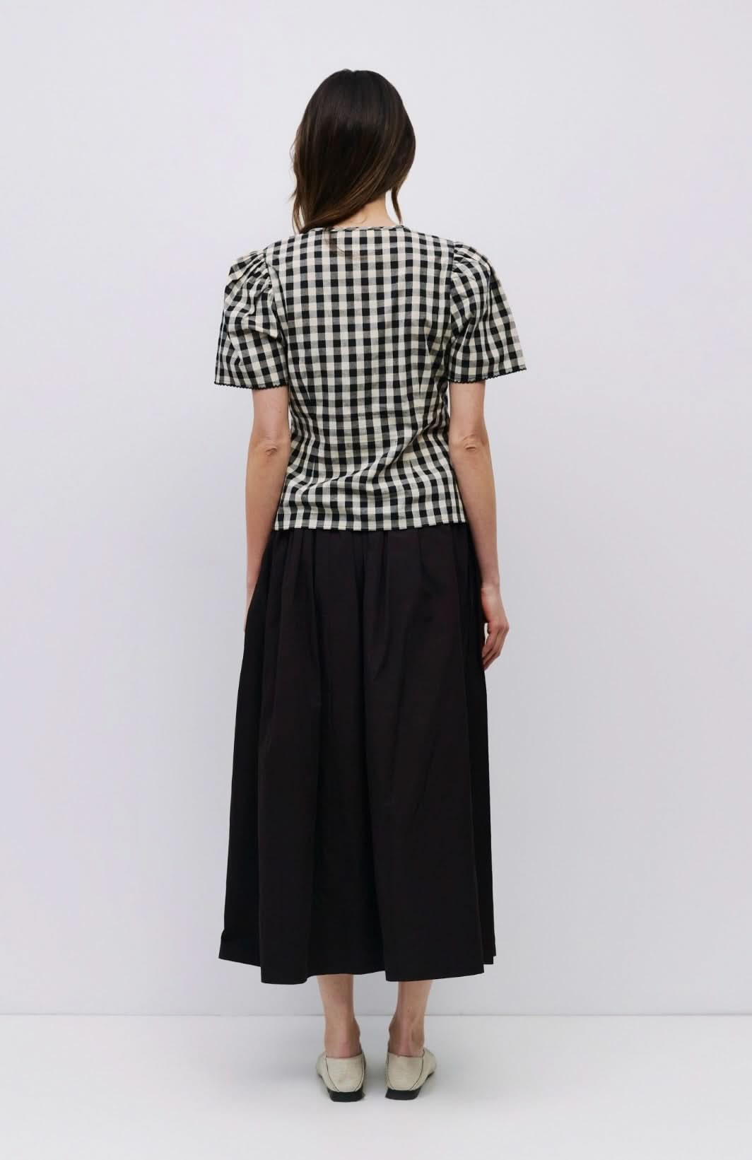 Woman facing backward wearing checkered puff sleeve blouse with black long skirt  