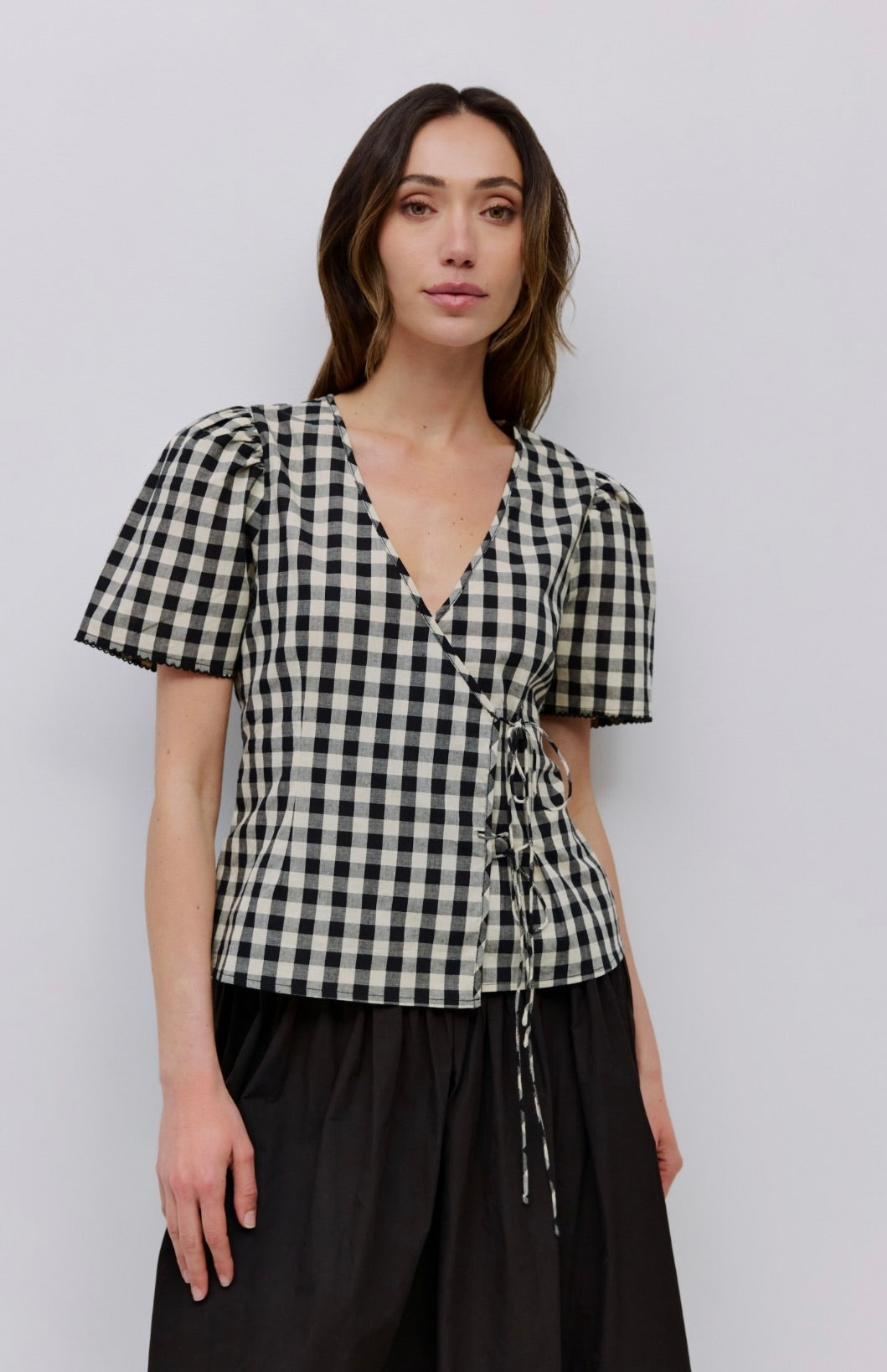 Woman wearing checkered puff sleeve blouse with 2 wrap ties in the front with black long skirt  