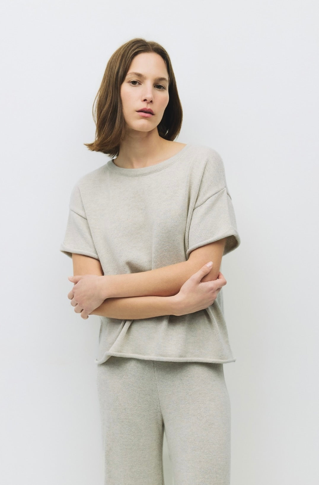 Woman wearing  oatmeal color knit shirt with a relaxed fit and raw roll-up hem and matching pants 