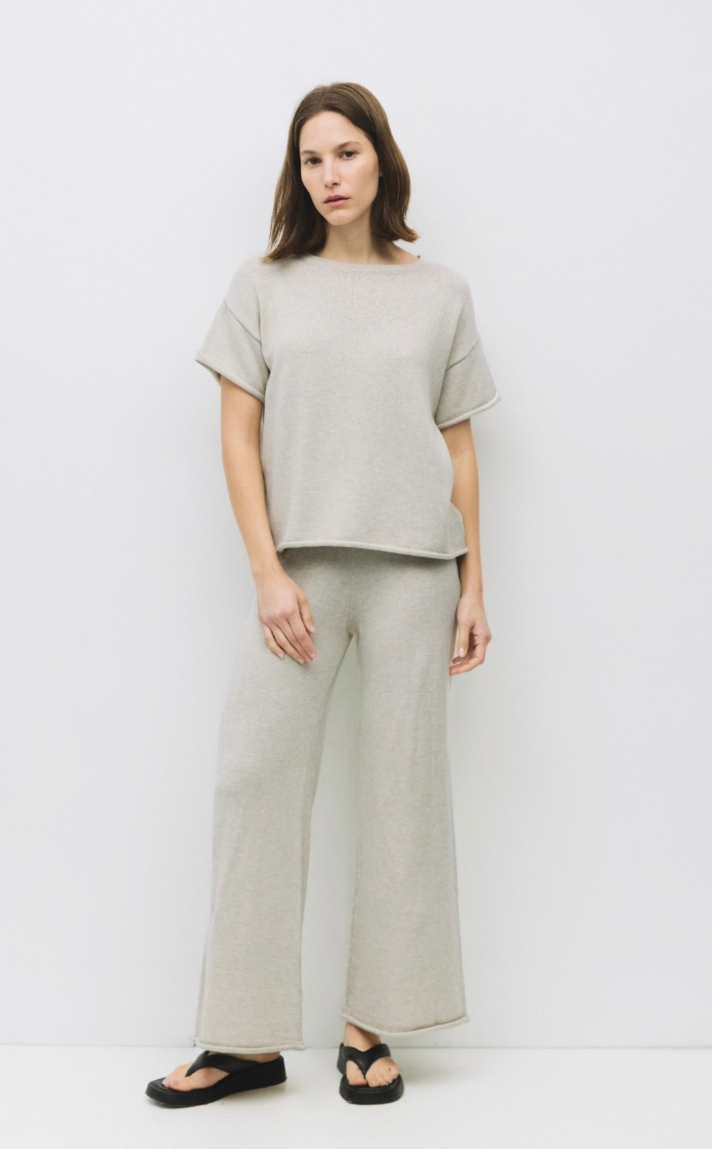 Woman wearing  oatmeal color wide-leg knit trousers with a relaxed fit and raw roll-up hem and matching shirt 