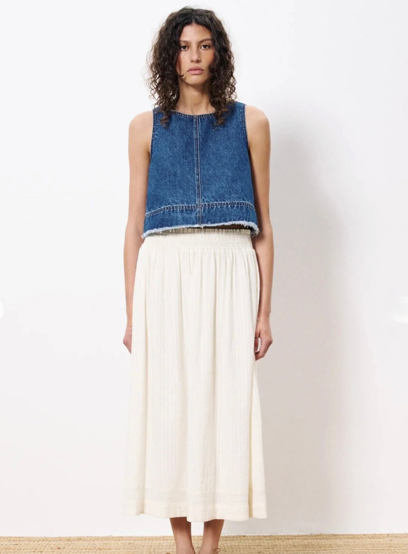 woman wearing cream colored maxi skirt with embroidered details and elastic waistband paired with jean sleeveless top 