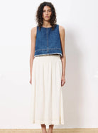woman wearing cream colored maxi skirt with embroidered details and elastic waistband paired with jean sleeveless top 