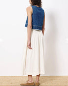 woman wearing cream colored maxi skirt with embroidered details and elastic waistband with jean vest top 