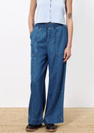 Woman wearing wide leg denim with elastic waistband, two front pockets, and two back patch pockets paired with light blue top and black shoes 