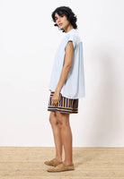Woman turned to the side wearing lightweight light blue blouse paired with tan and black dress shorts 