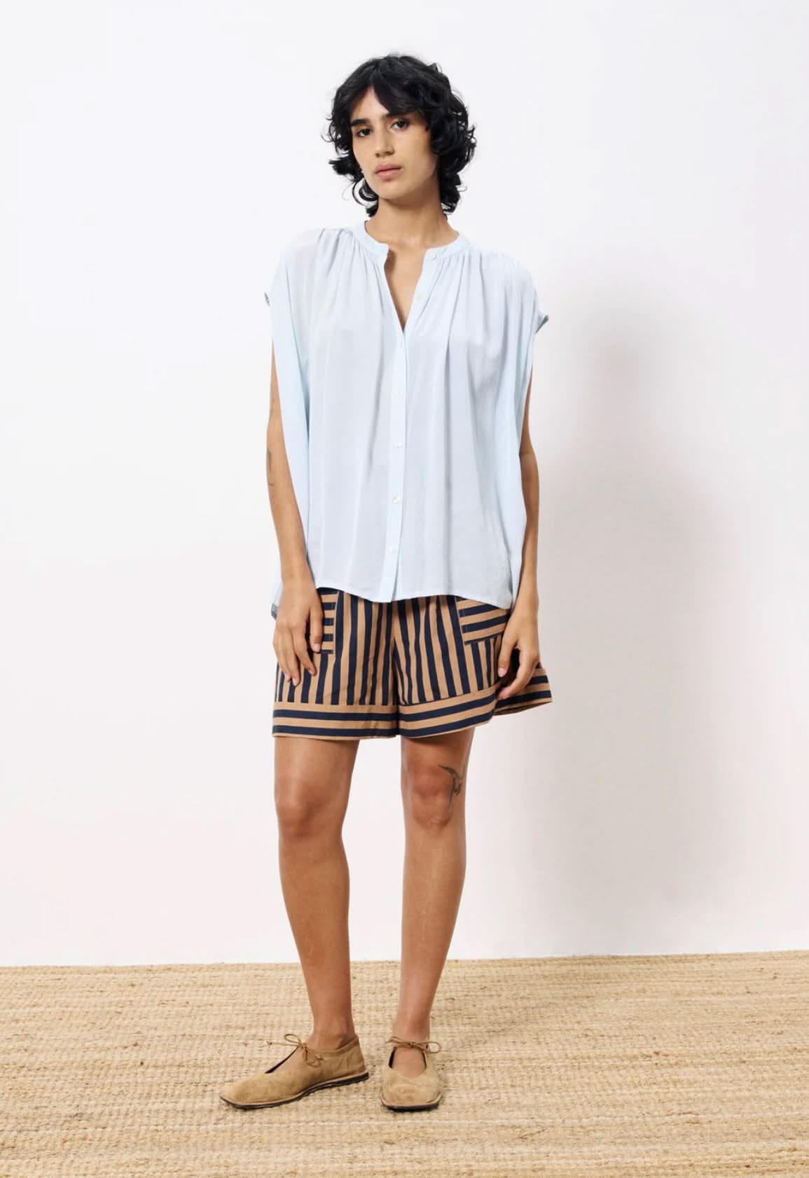 Woman  wearing lightweight light blue blouse button closure paired with tan and black dress shorts 