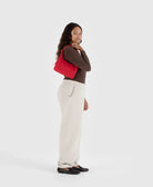 Woman wearing neutral colors carrying Bright candy apple red BAGGU mini nylon shoulder bag on her shoulder 