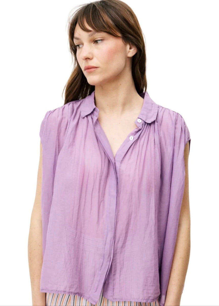 Woman wearing purple silky cotton button up, purple blouse, standing against white wall 