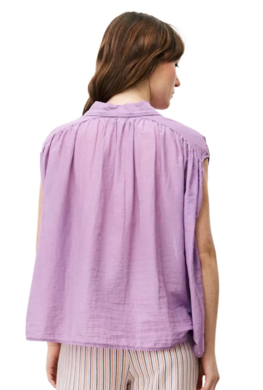 Woman wearing purple silky cotton button up, purple blouse, standing against white wall 