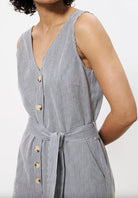 Woman wearing vertically pinstriped grey and white jumpsuit with buttons down the front and a tie around waist 