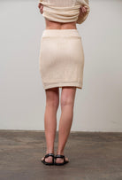 Woman facing away from the camera wearing cream beige drawstring crochet mini skirt