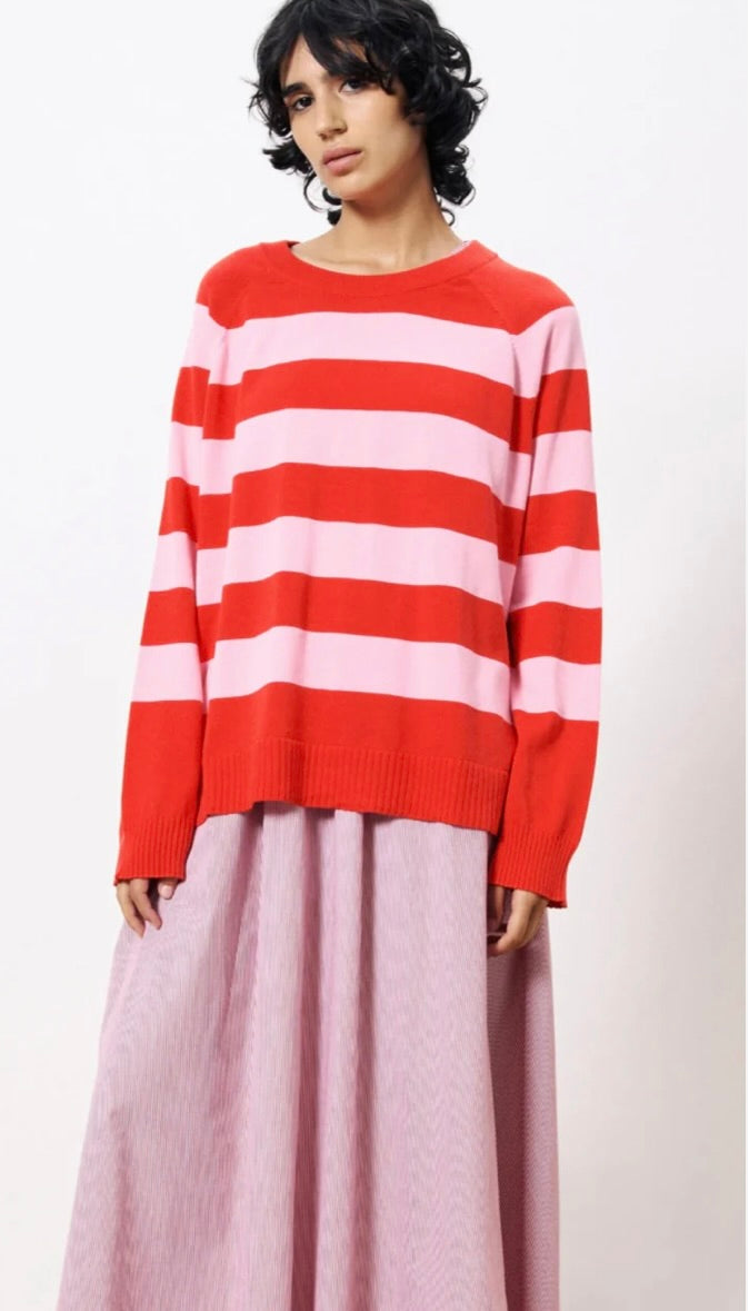Woman wearing pink and red horizontal thick striped sweater standing against a blank wall 