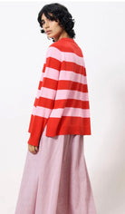 Woman wearing pink and red horizontal thick striped sweater standing against a blank wall 