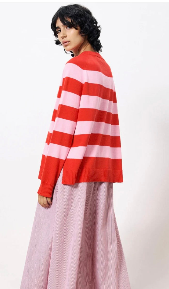 Woman wearing pink and red horizontal thick striped sweater standing against a blank wall 