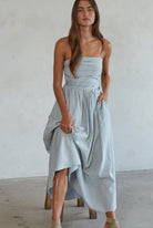 Woman wearing white and green/blue vertically striped, sleeveless maxi dress standing against a blank wall