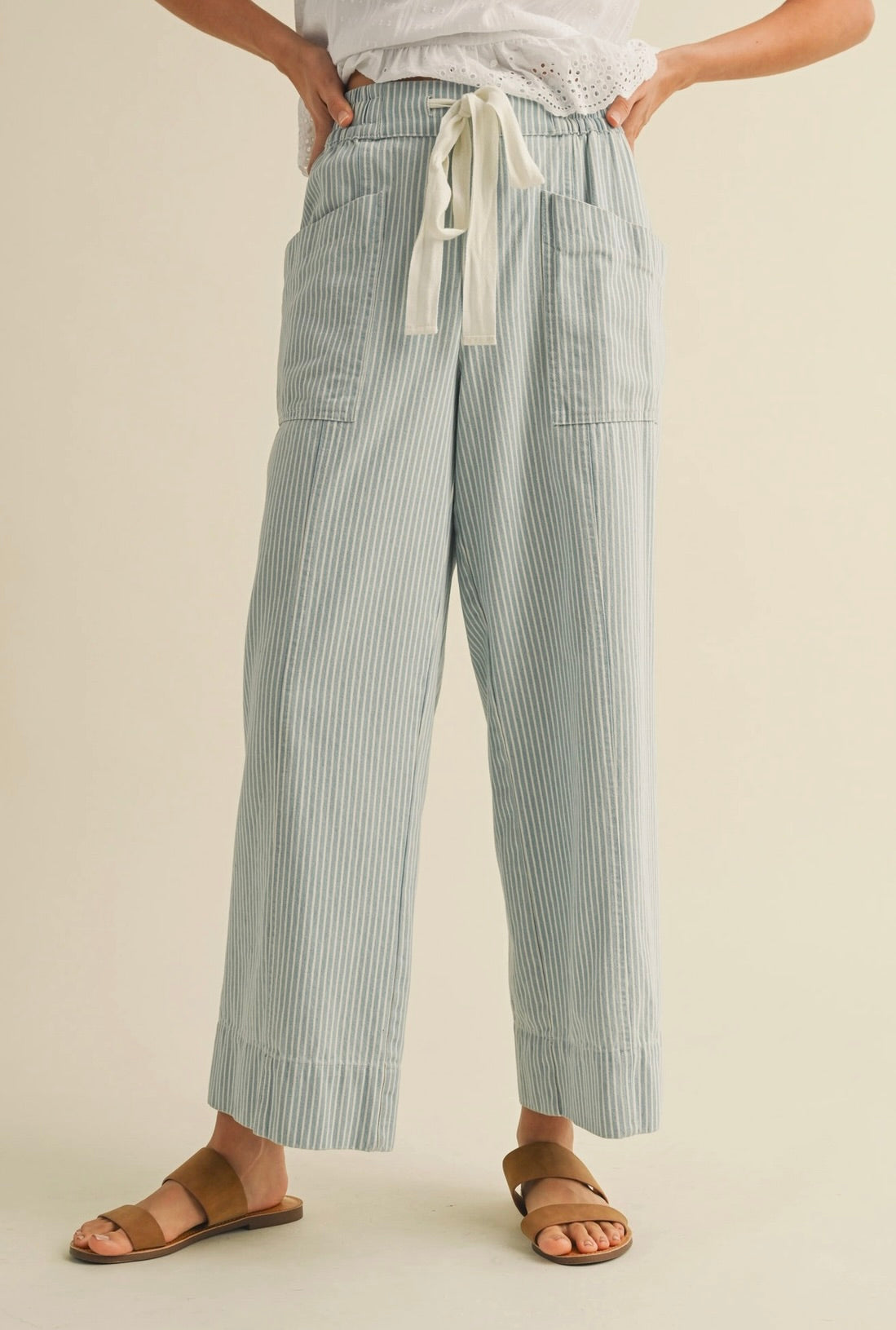 Woman wearing white blouse with cropped blue vertically striped summer pants with waist tie 