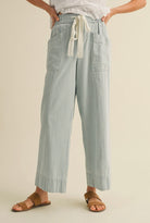 Woman wearing white blouse with cropped blue vertically striped summer pants with waist tie 