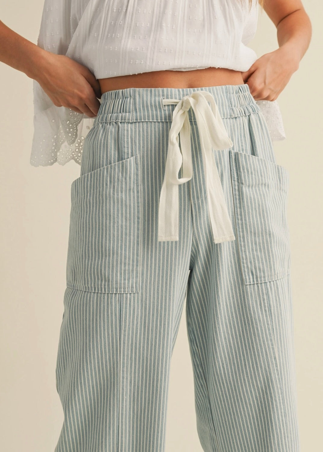 Woman wearing white blouse with cropped blue vertically striped summer pants with waist tie 