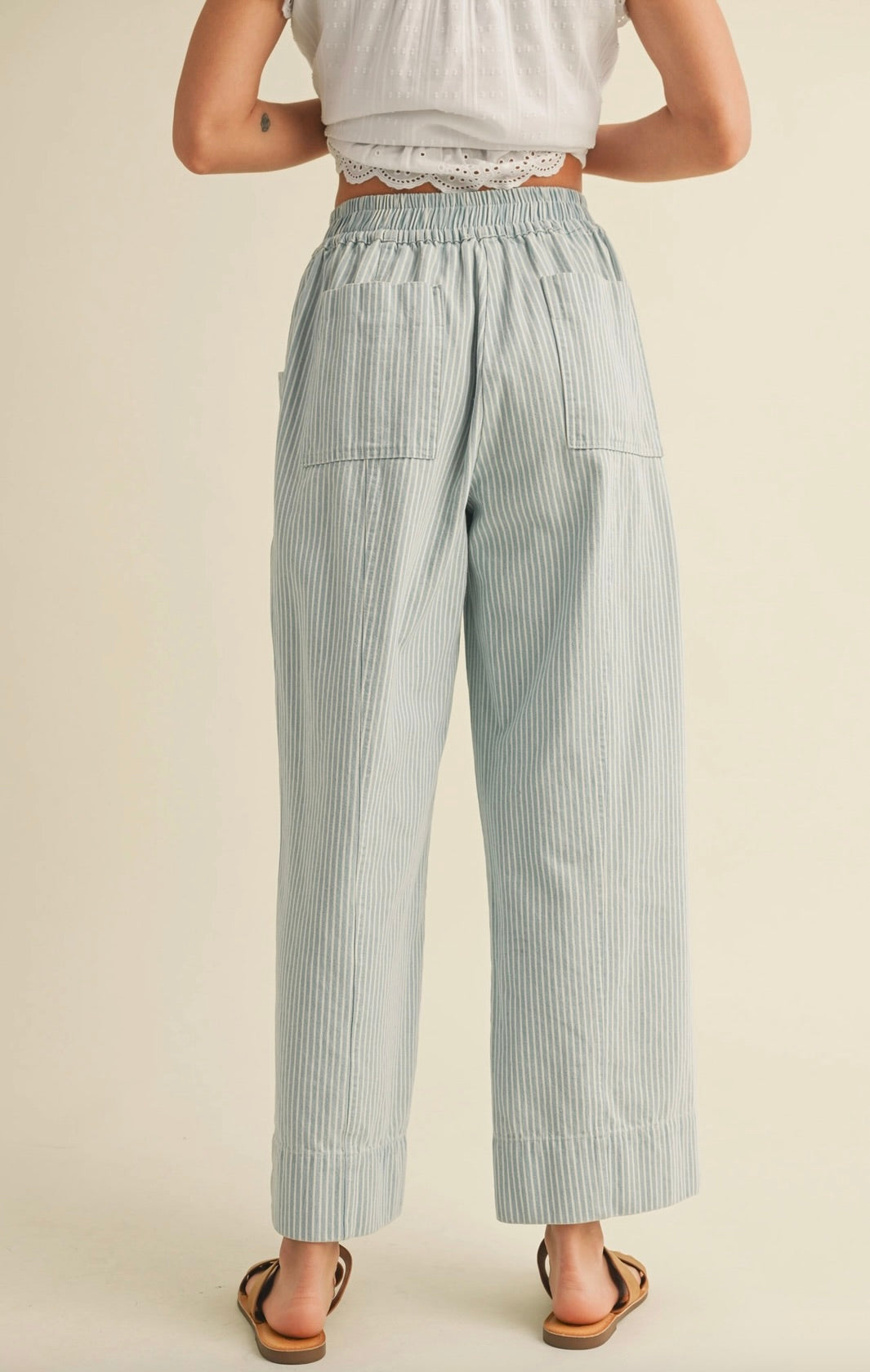 Woman wearing white blouse with cropped blue vertically striped summer pants with waist tie 
