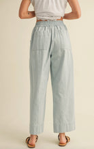 Woman wearing white blouse with cropped blue vertically striped summer pants with waist tie 