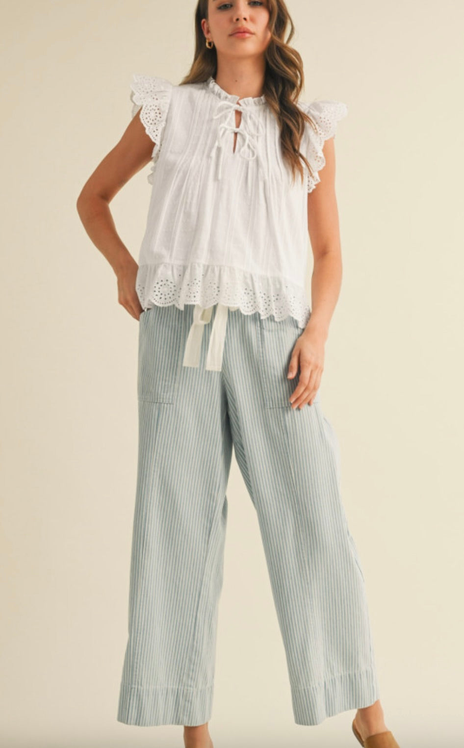Woman wearing white blouse with cropped green vertically striped summer pants with waist tie 