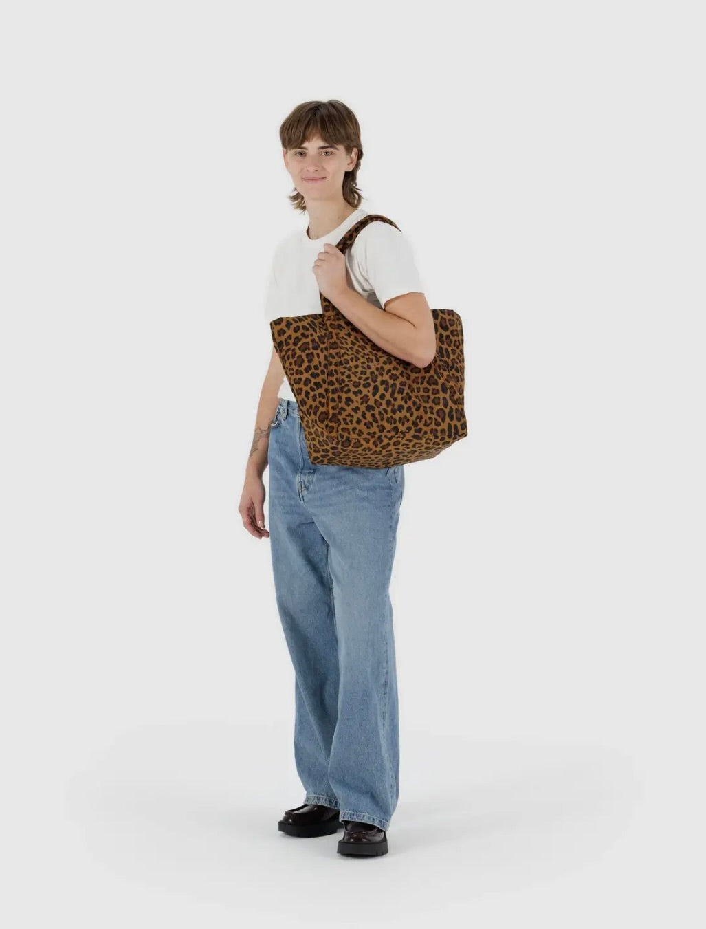 Man holding a large leopard tote bag on a white background. 