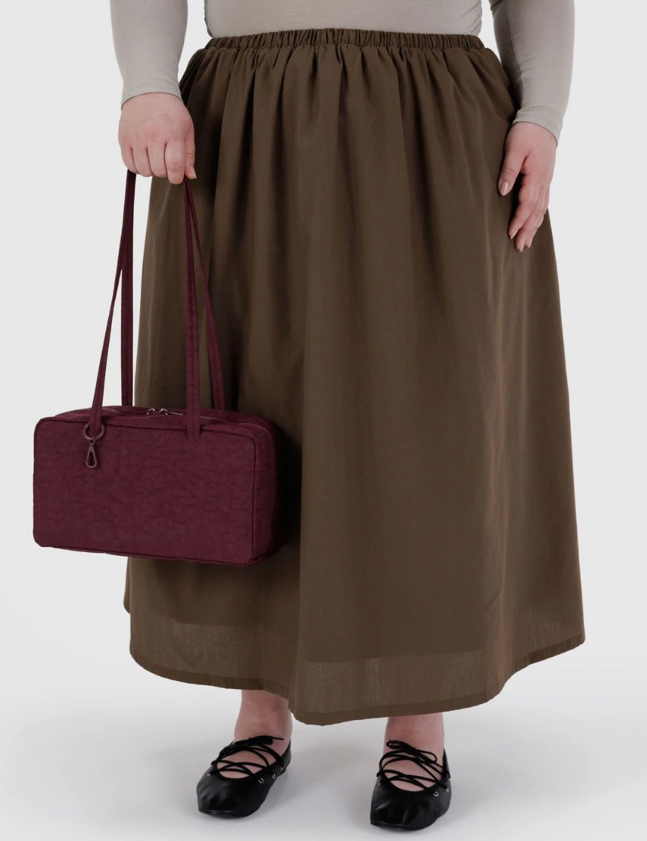 Person wearing a brown skirt holding a maroon handbag on a white background