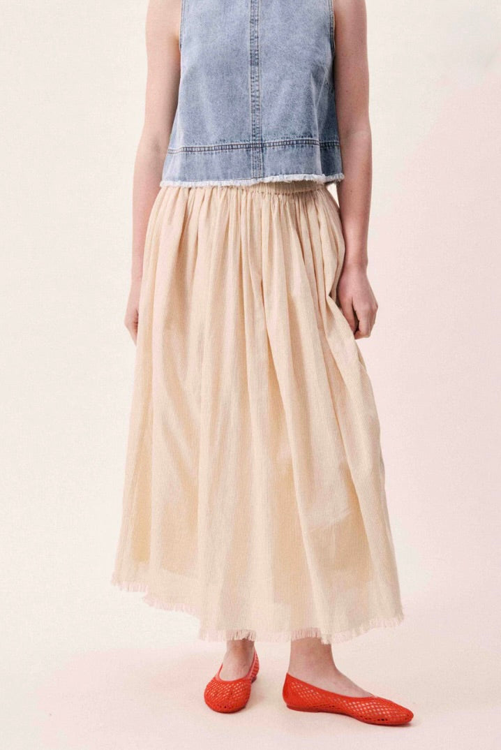 Person wearing a denim top and beige skirt on a plain background