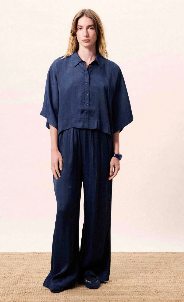 Woman wearing a navy blue outfit with a matching shirt and wide-leg pants on a light pink background.