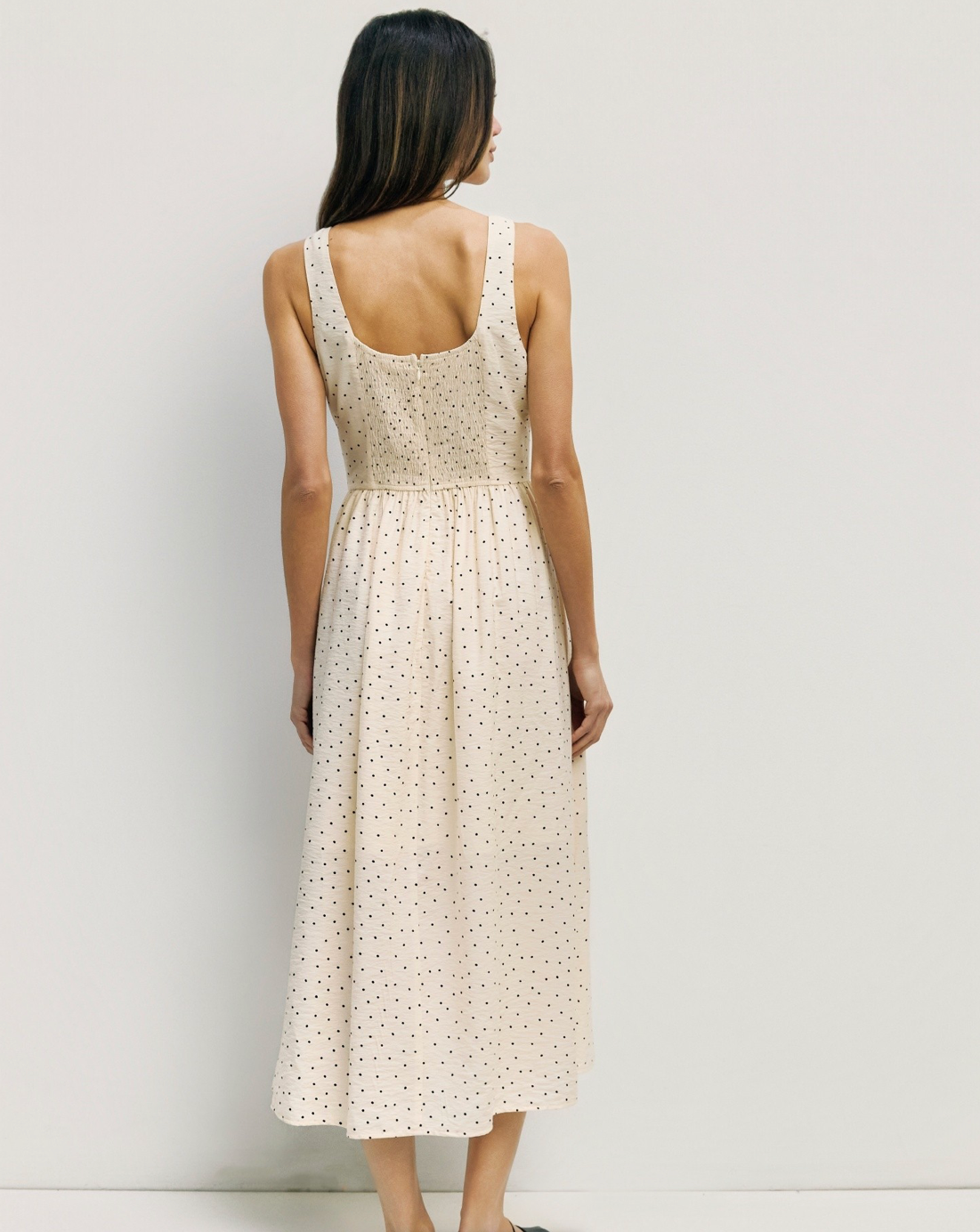 Woman wearing a beige sleeveless dress with a subtle pattern against a plain background