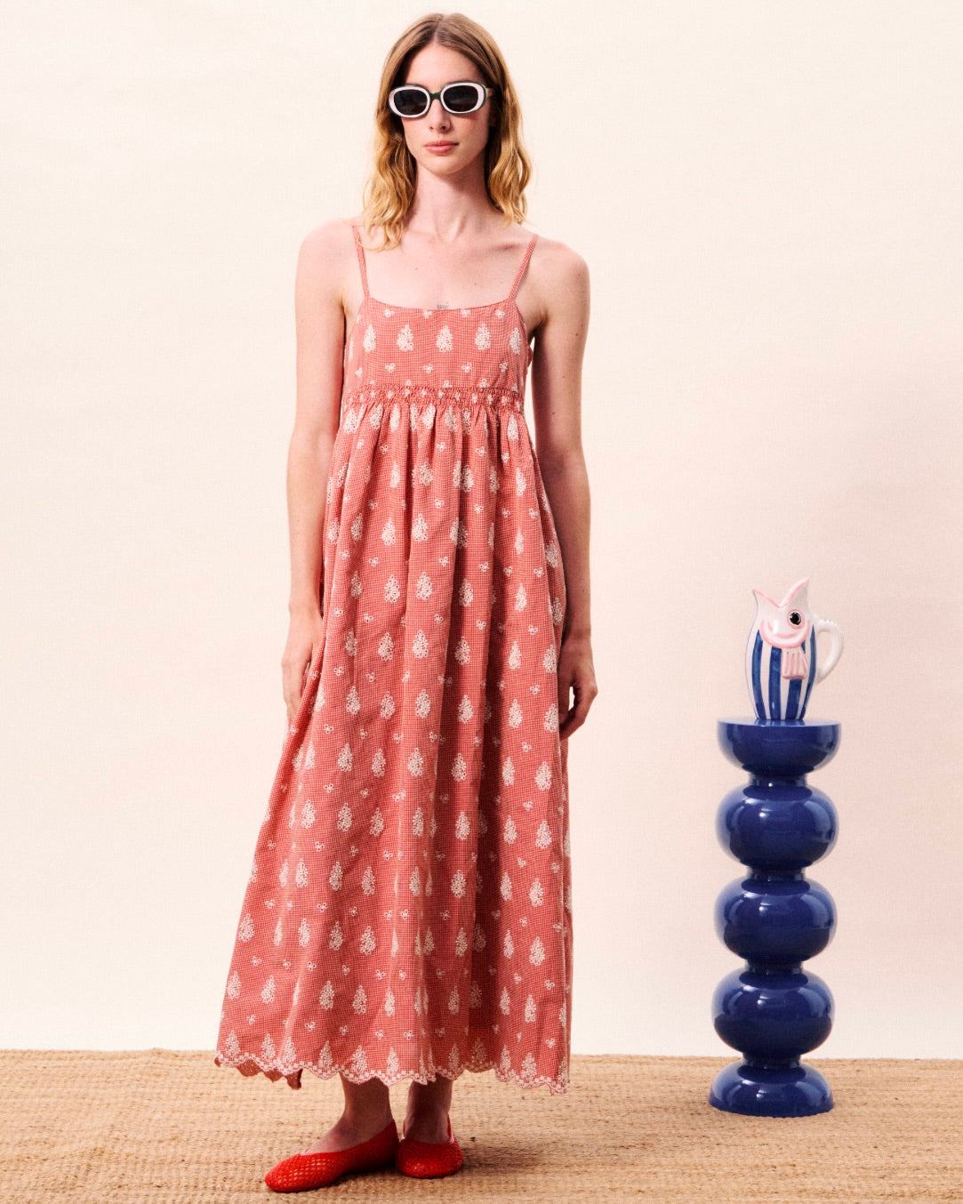 Woman wearing a pink floral dress standing next to a blue decorative vase on a beige surface.