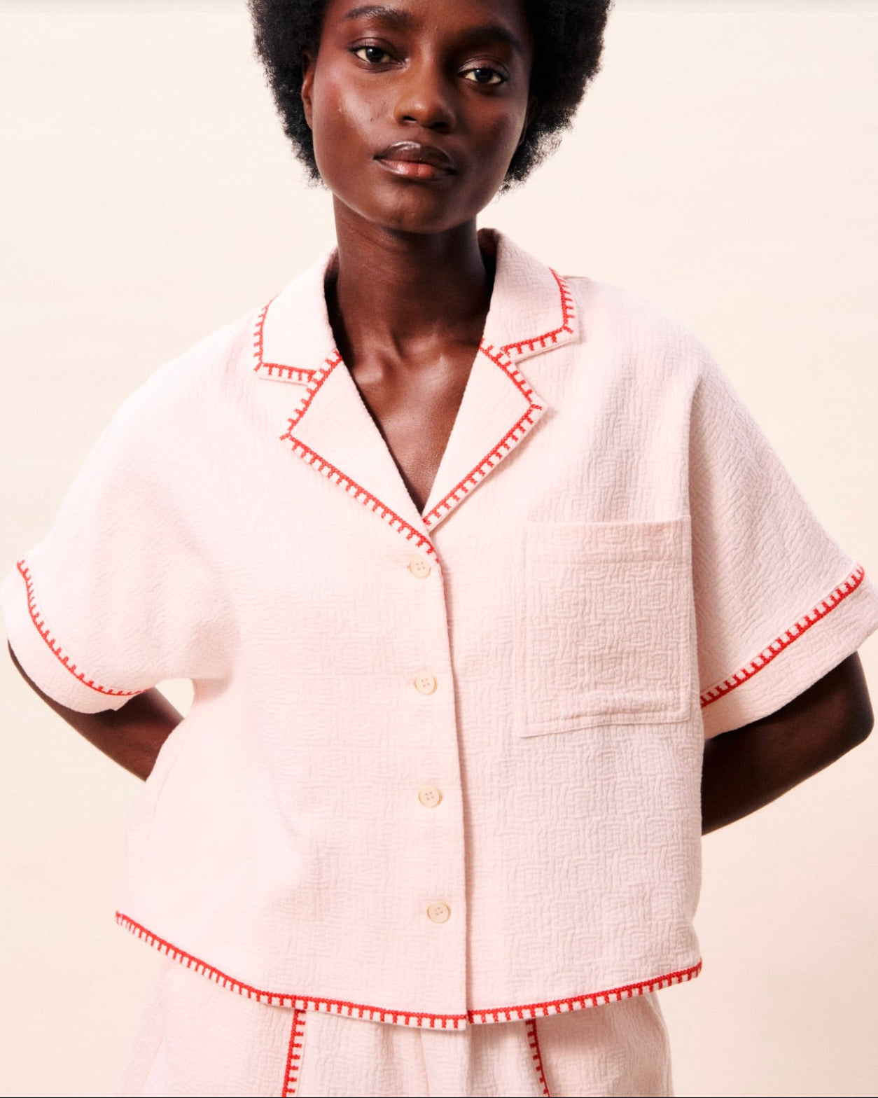 Woman wearing a white outfit with red trim on a plain background