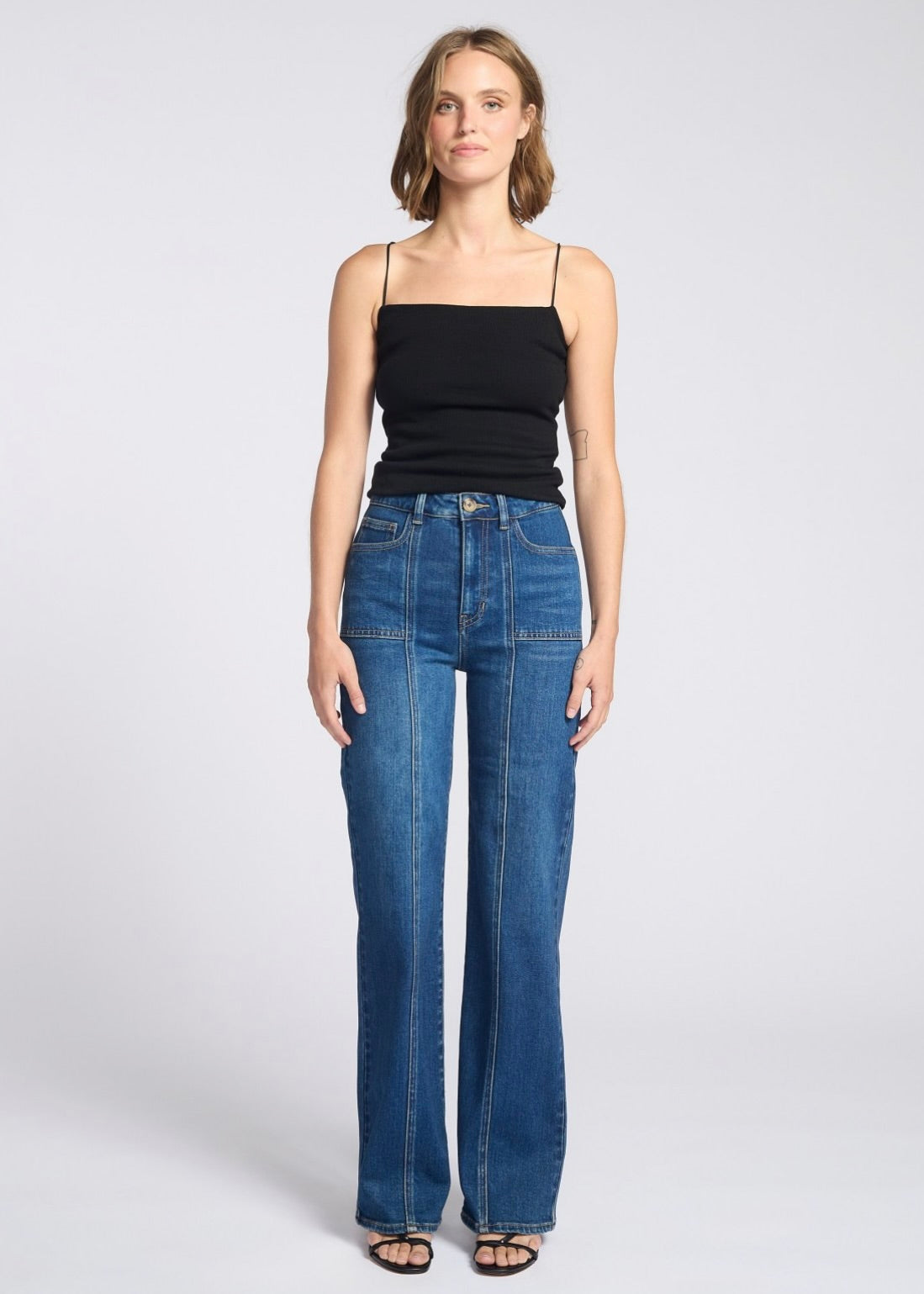 Woman wearing blue jeans and a black top on a white background