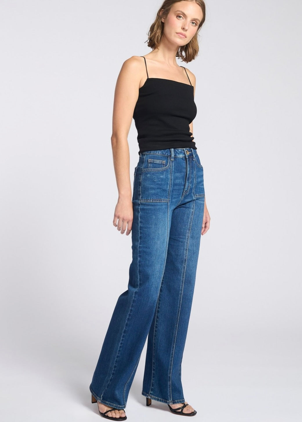 Woman wearing blue jeans and a black top on a white background