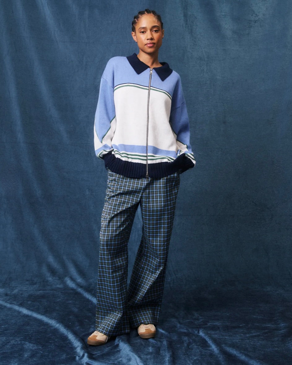 Person wearing a blue and white sweater with plaid pants on a blue background