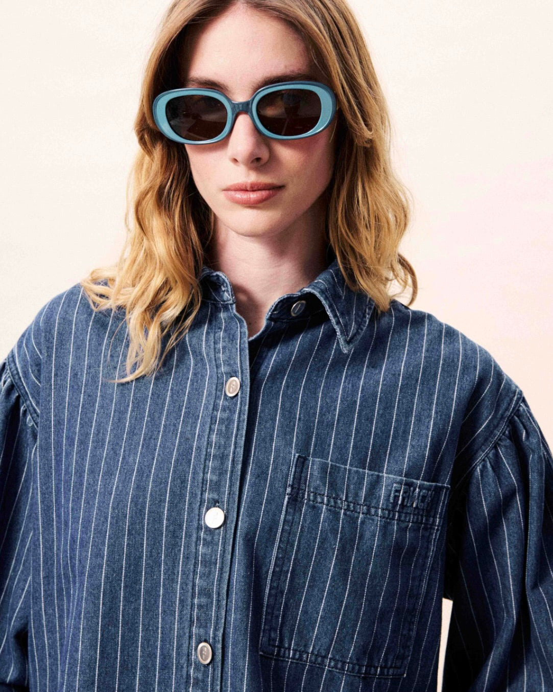 Person wearing a blue pinstripe shirt and sunglasses against a light background