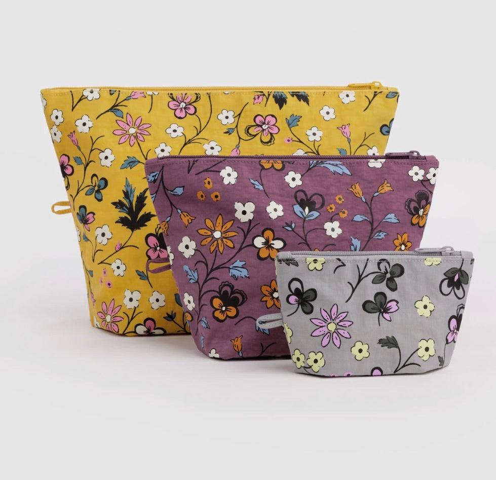 Three fabric zip pouches with floral prints in yellow, mauve, and light gray, arranged by size on a white background.