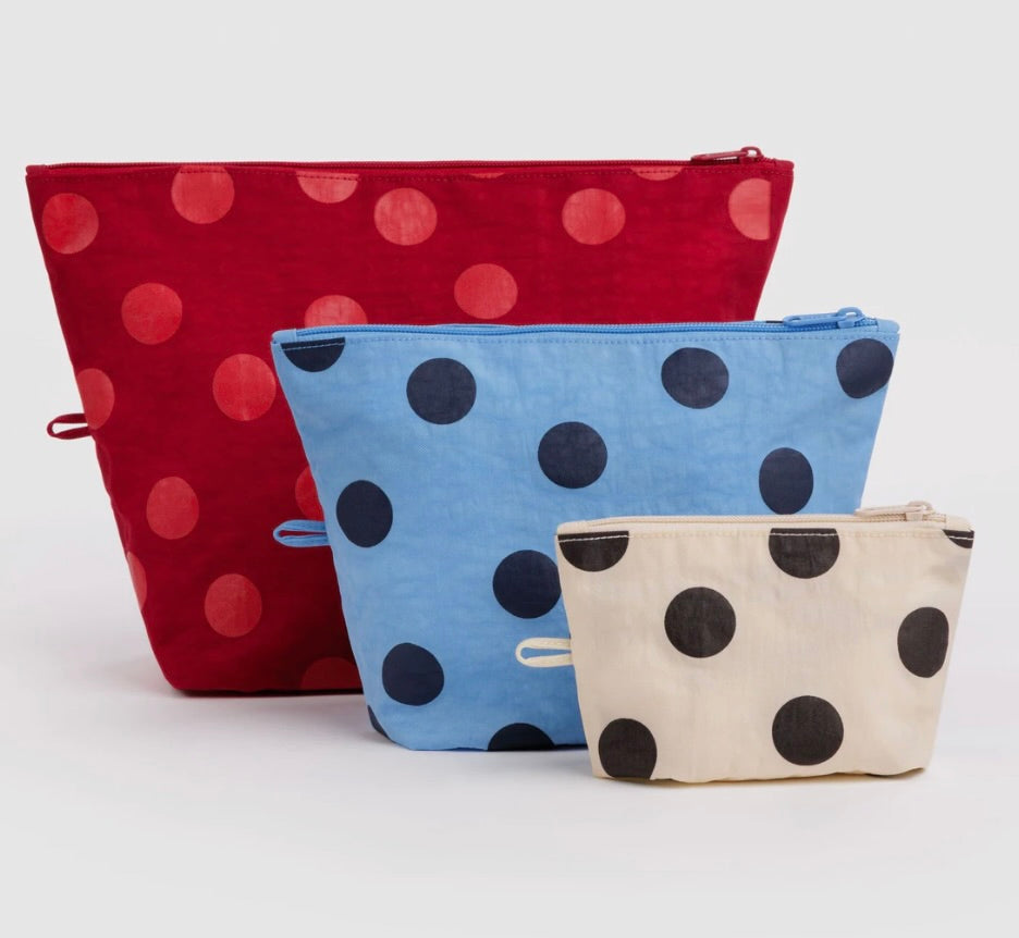 Three fabric zip pouches with a polka dot pattern, displayed in a size gradient. The largest pouch is red with pinkish-red dots, the middle pouch is light blue with dark blue dots, and the smallest pouch is cream with dark brown dots.