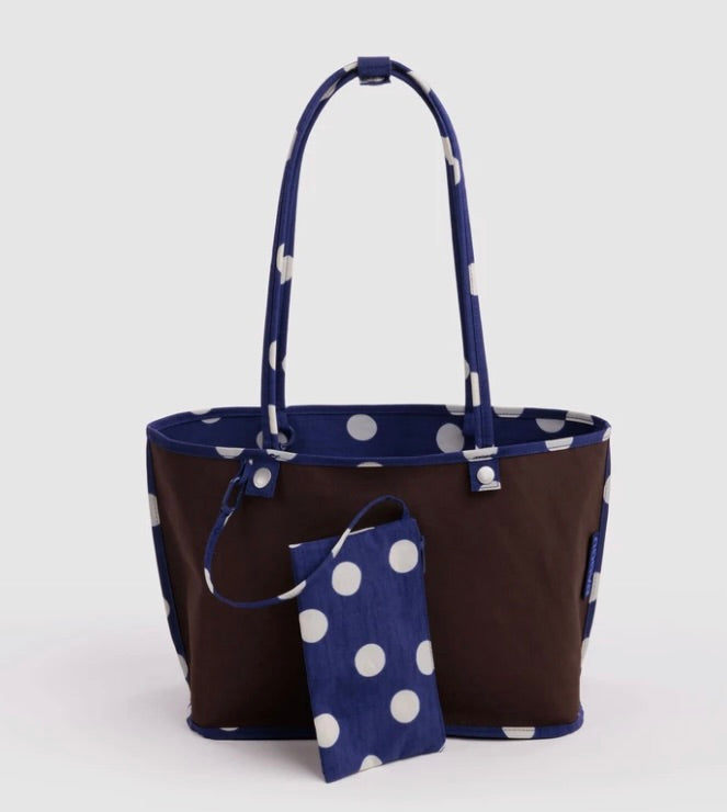 A dark brown canvas tote bag with navy blue handles and trim, featuring a white polka dot pattern. A matching small zippered pouch with the same navy and white polka dot fabric is placed in front of the bag against a light gray background.