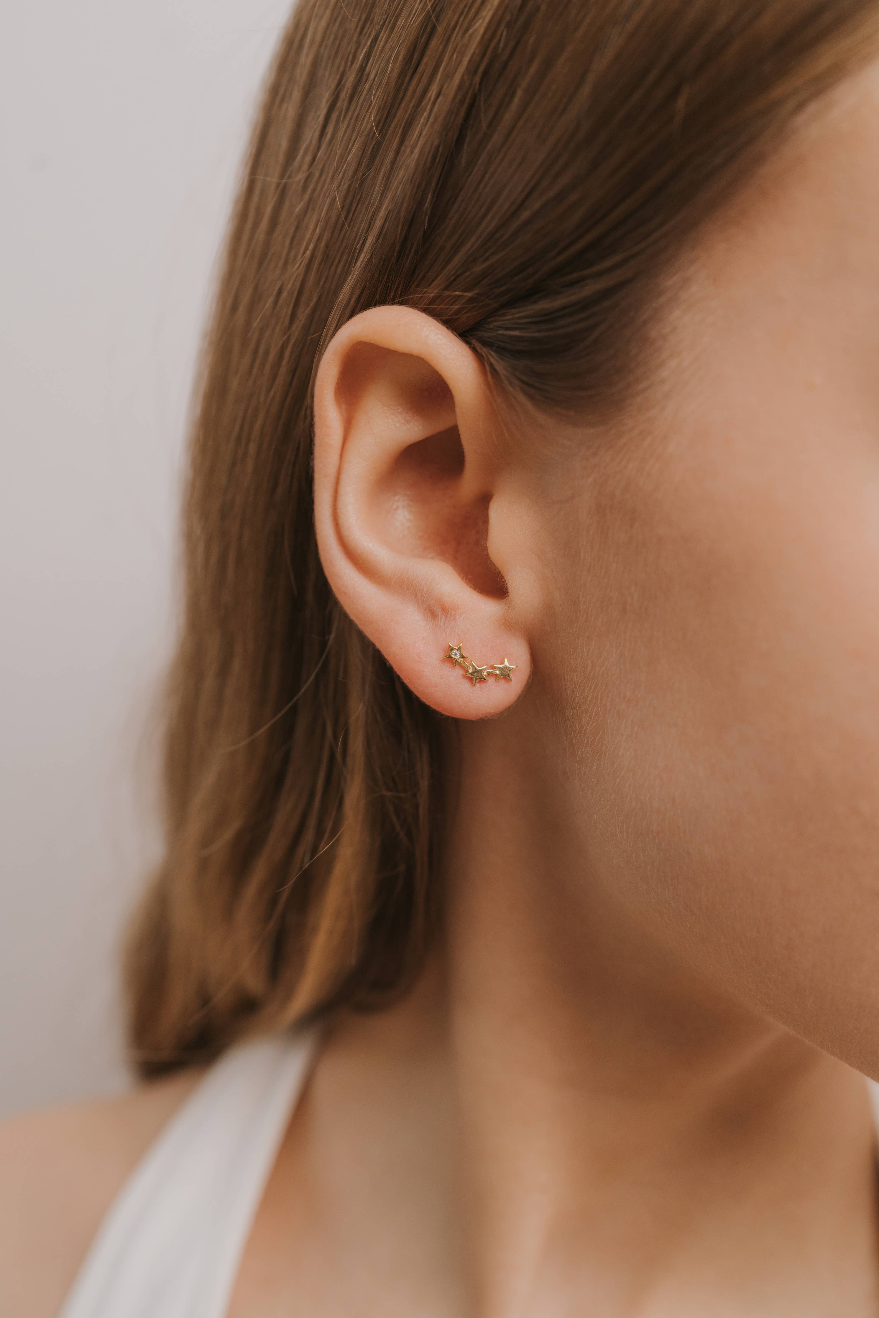 Close-up of an ear wearing a small gold earring stars earings