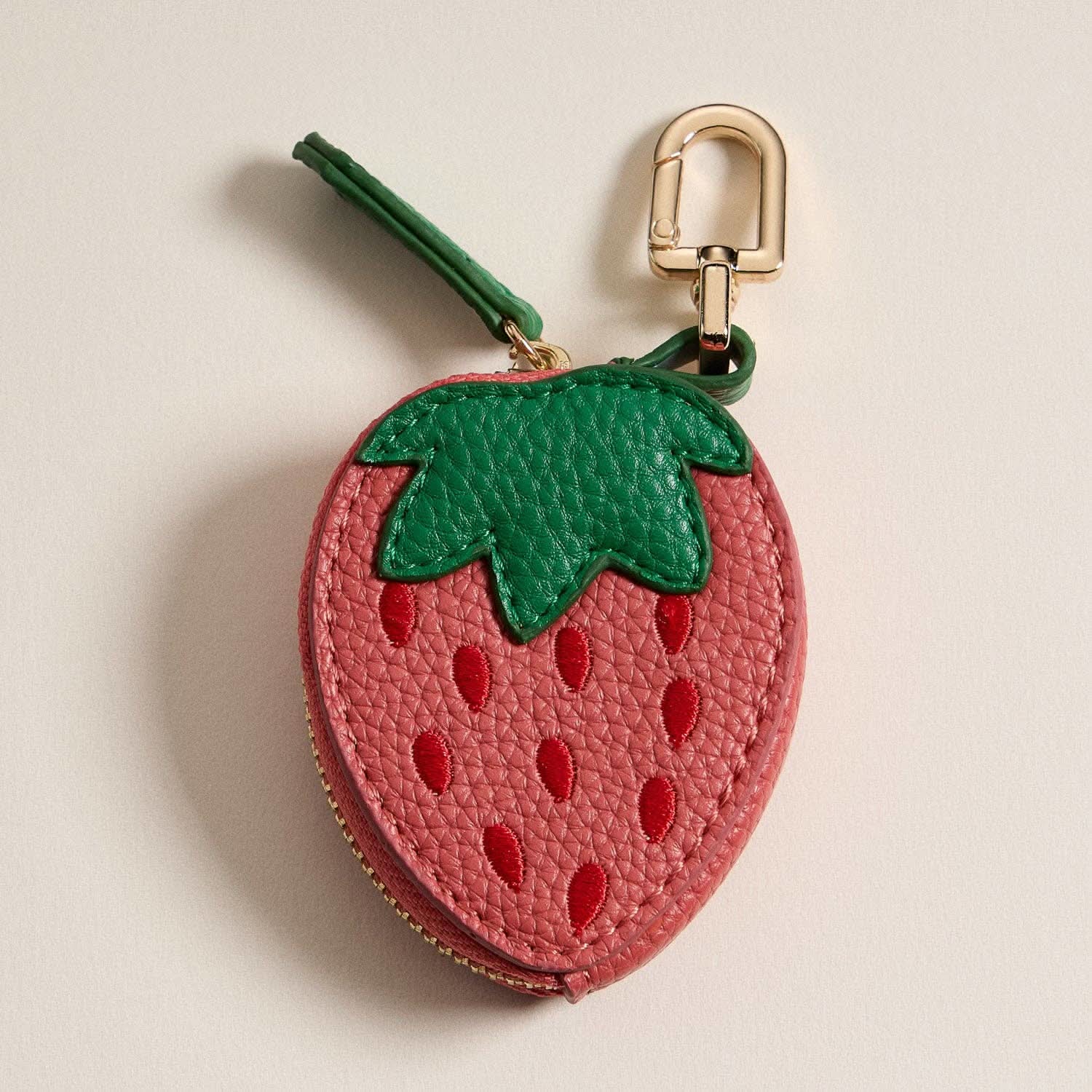 Strawberry-shaped keychain with a gold clasp on a beige background