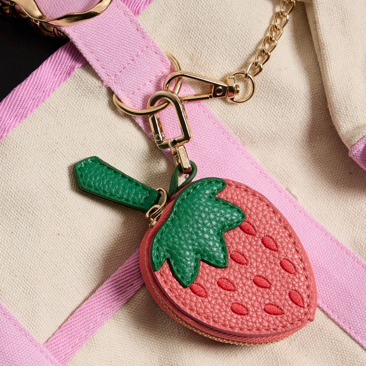 Strawberry-shaped keychain attached to a pink strap on a beige background